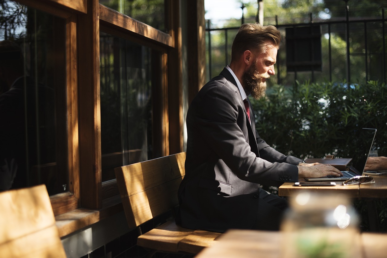well-dressed man in a dark suit working on a laptop at an outdoor wooden table.